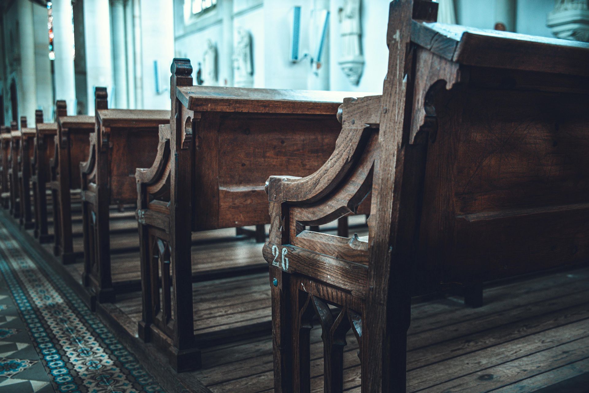 Rows of empty wooden church pews beside a patterned aisle runner in a dim sanctuary