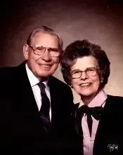 Smiling older couple in formal attire posing against a dark studio background