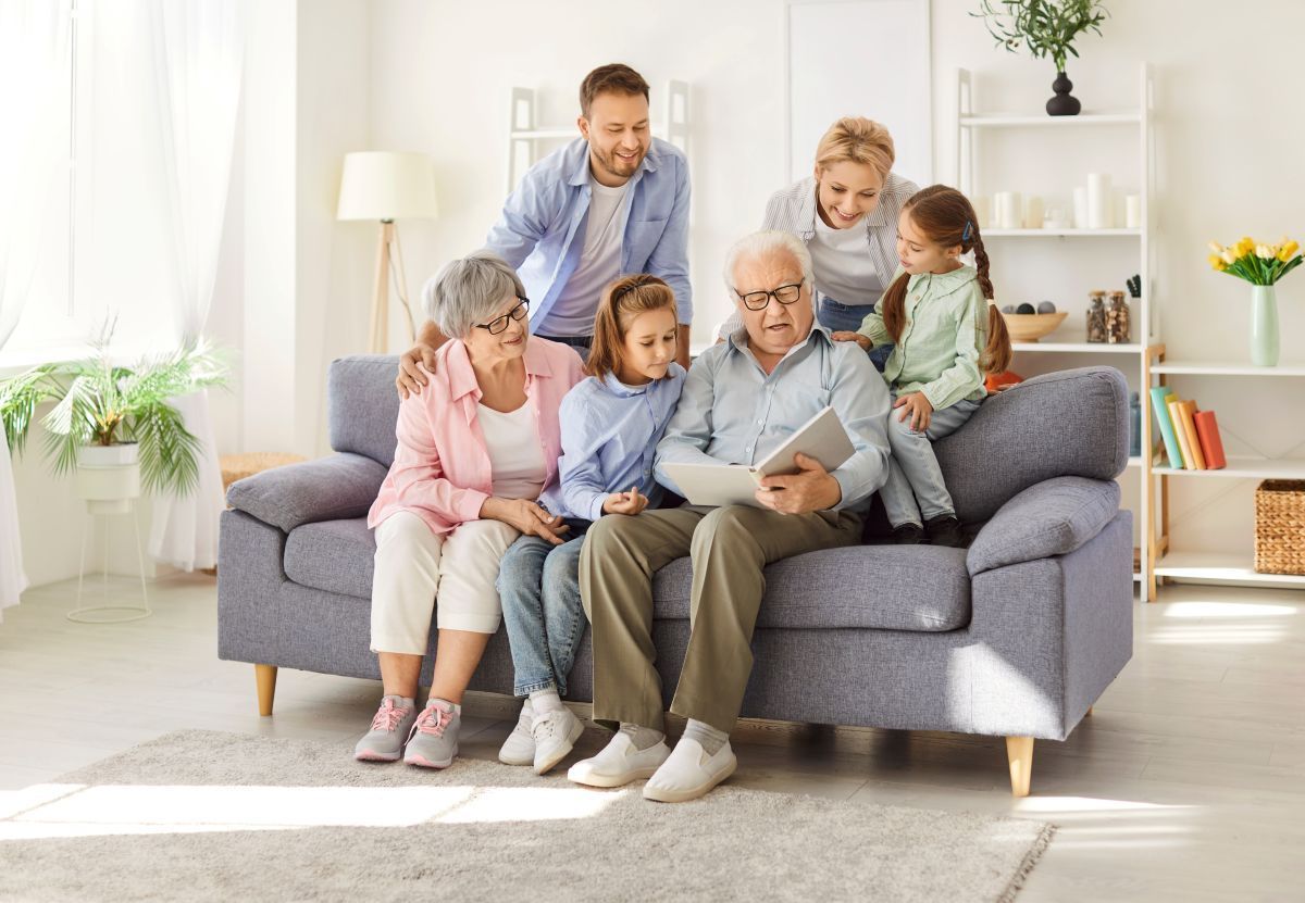 Family gathered on a gray sofa in a bright living room, reading a book together