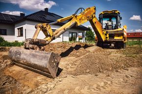 Yellow excavator leveling dirt in a residential yard beside a house under construction