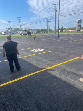 People standing in a marked parking lot near a road and utility poles on a sunny day