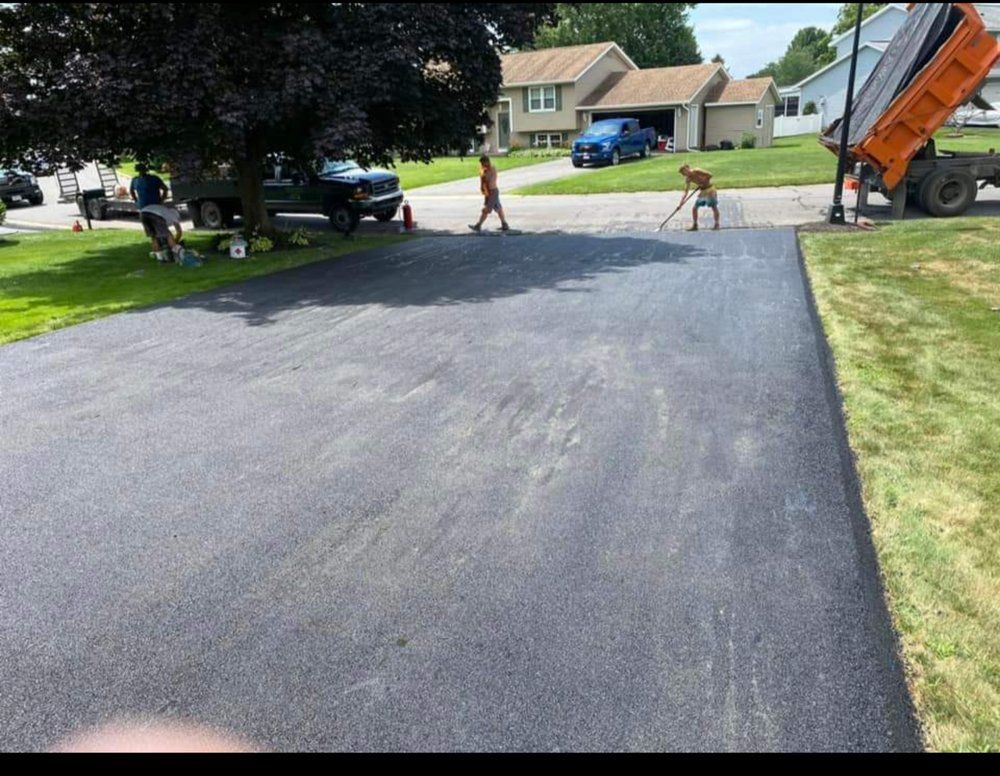 Freshly paved driveway with workers, dogs, and a truck in a suburban neighborhood