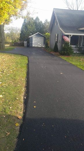 Driveway leading to a white garage beside a house with an American flag and autumn trees.