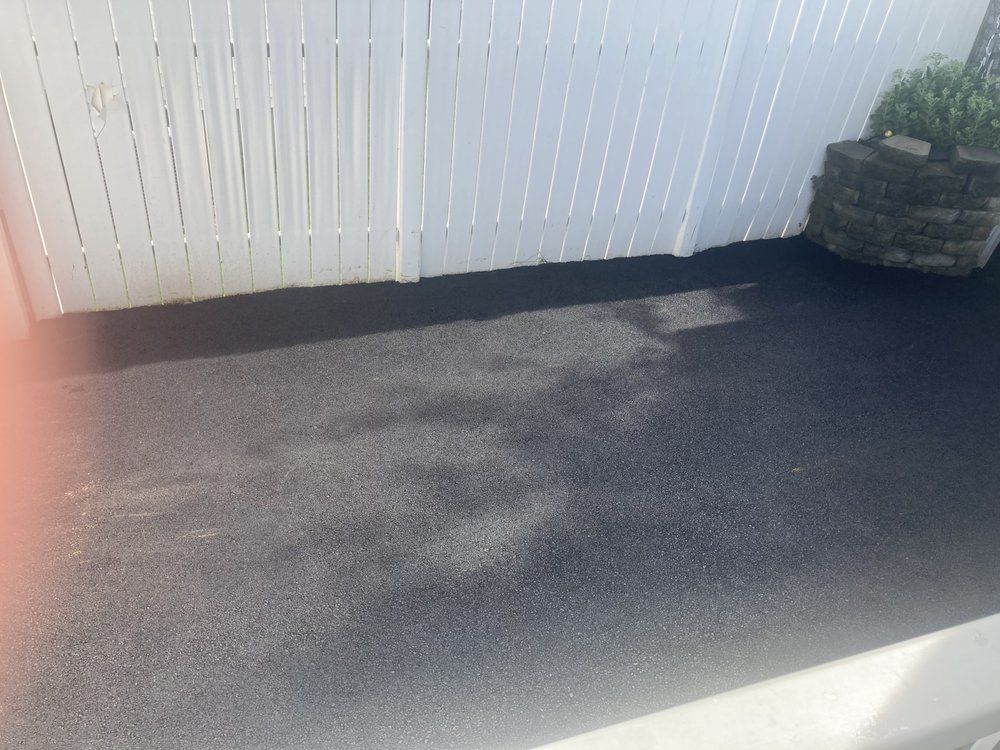 Sunlit paved patio beside a white fence, with a stone planter in the corner.