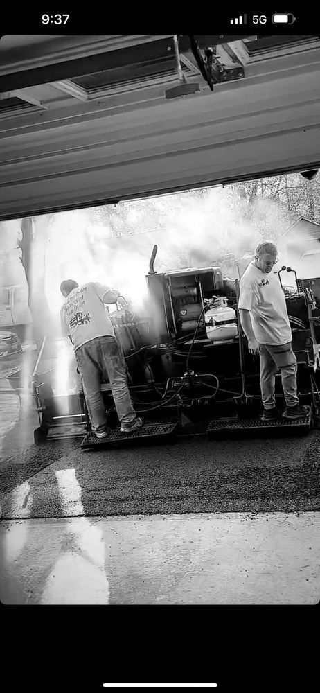 People standing around equipment under a covered area, one person bent over a table or cart.
