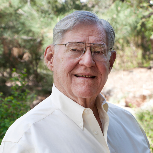 Smiling man in a white shirt standing outdoors with trees in the background