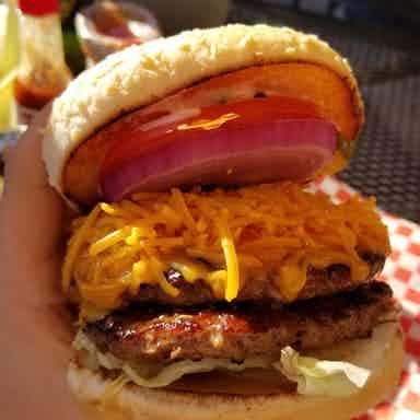 A person is holding a hamburger with cheese , tomatoes , onions and lettuce.