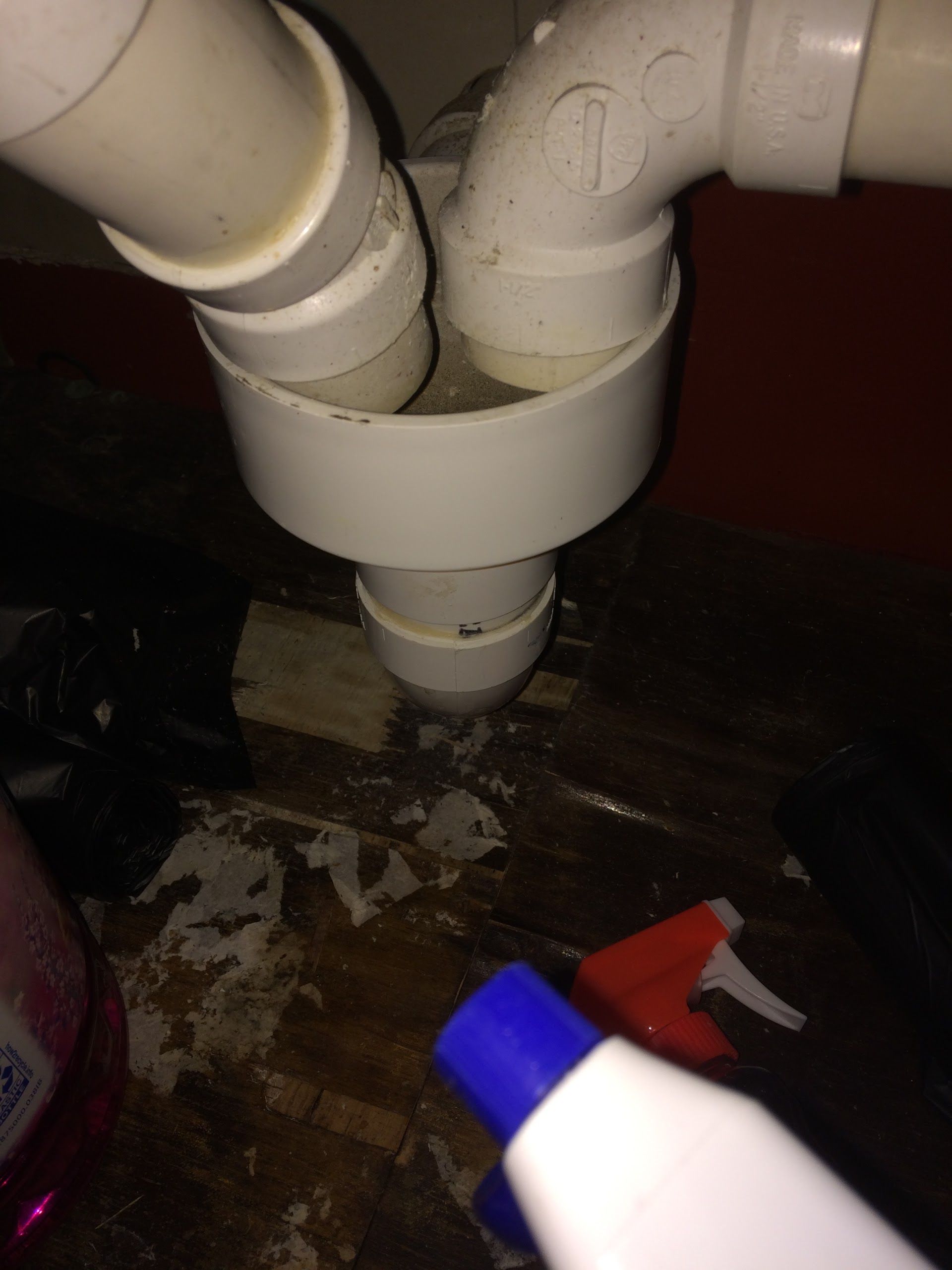 A close-up of two white PVC pipes discharging into an open-top floor drain assembly beneath a cabinet.