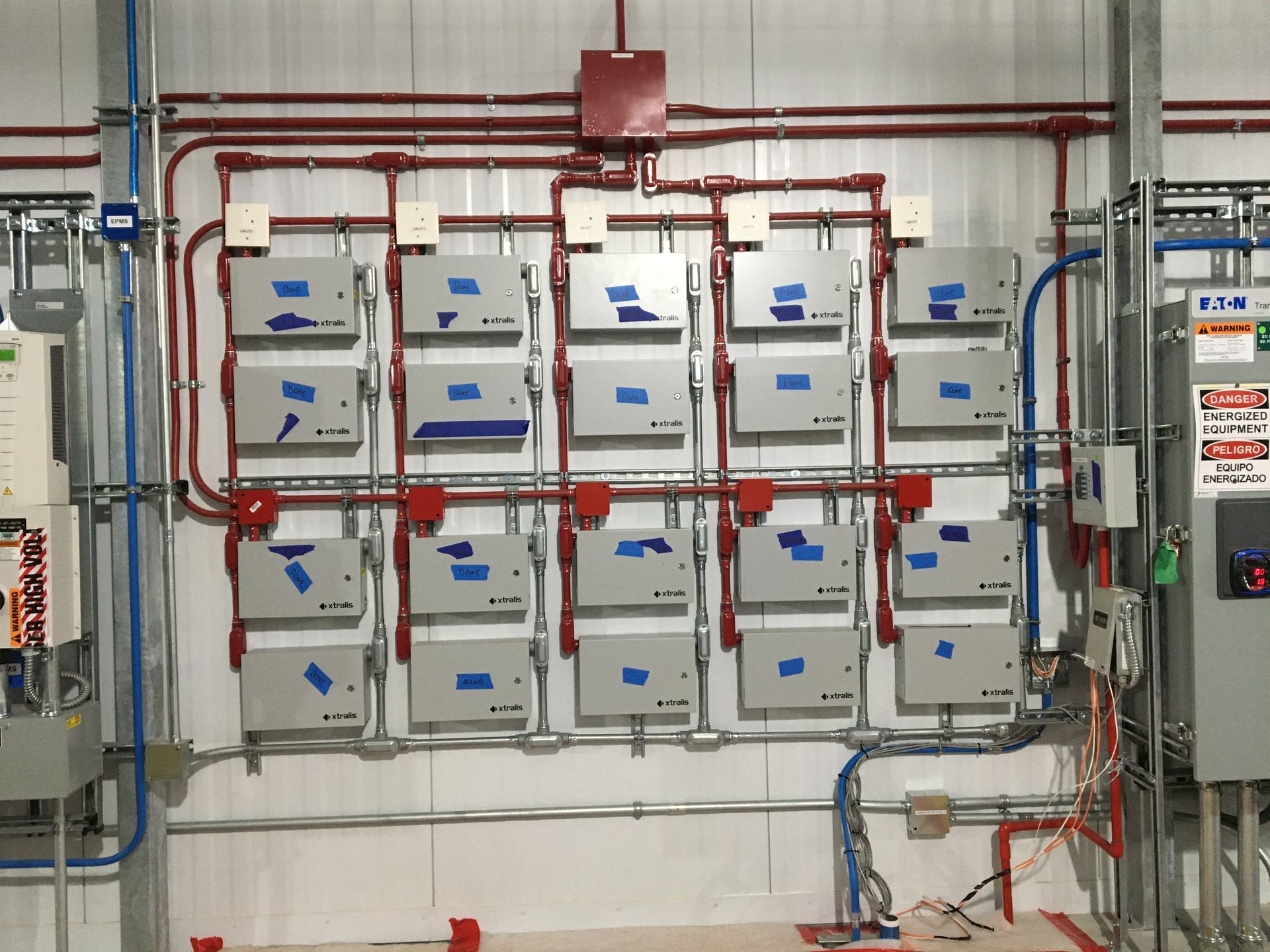 A wall-mounted electrical array featuring multiple grey rectangular enclosures connected by a network of red conduit pipes.