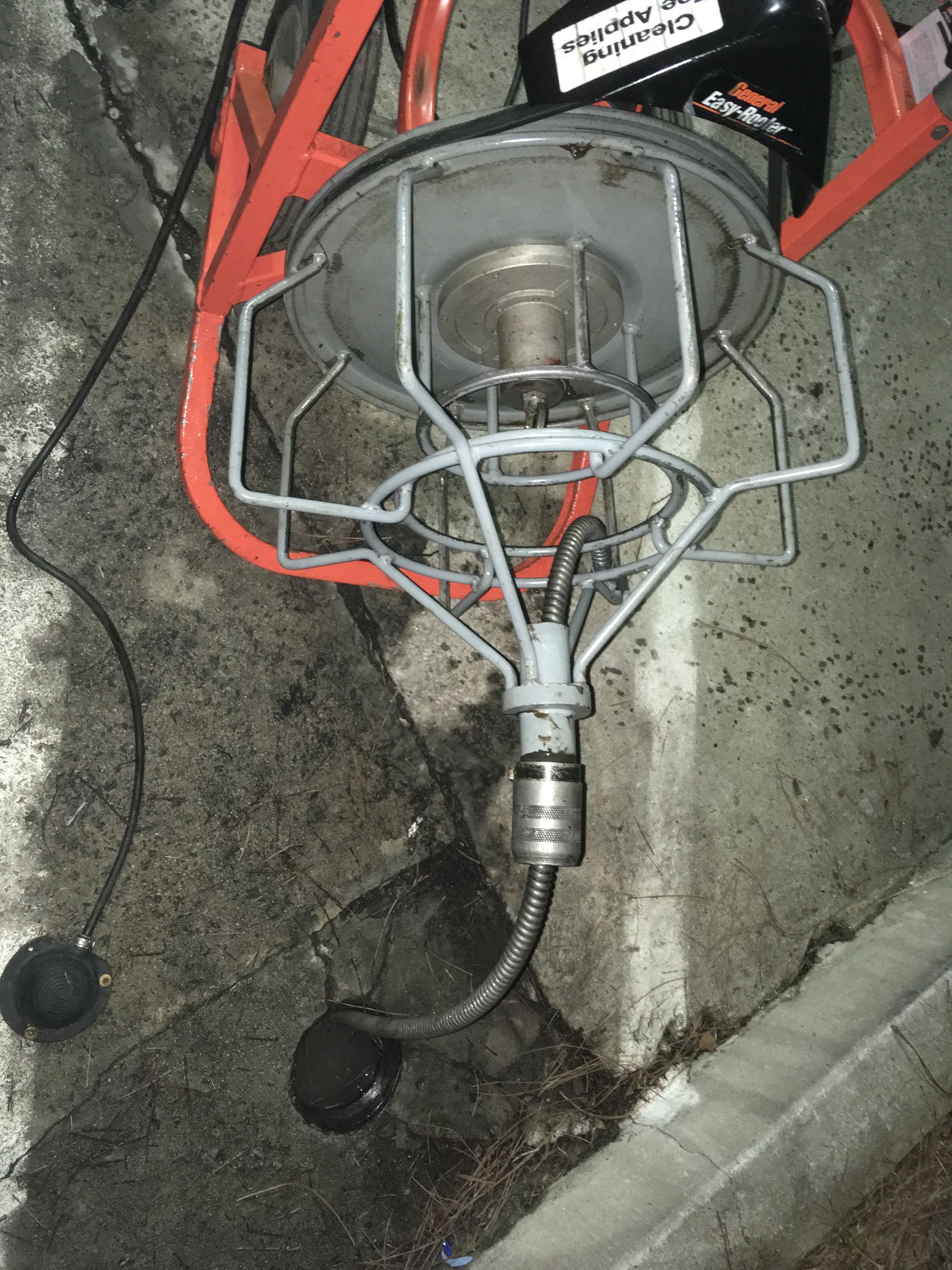 A portable halogen work light with a metal safety cage, resting on a concrete surface next to a curb.