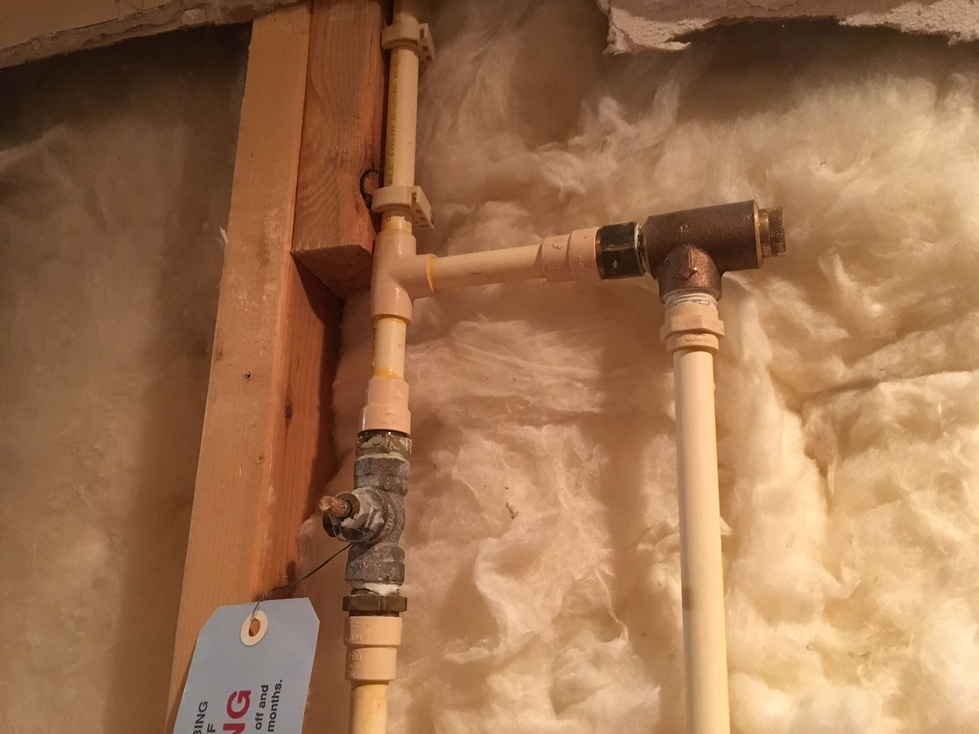 A plumbing setup with off-white CPVC pipes, metal fittings, and a shut-off valve, installed against a wooden stud.