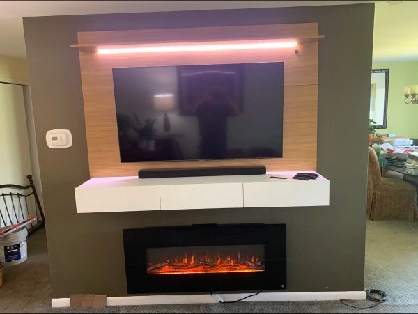 TV mounted on a wooden frame with a soundbar, floating shelf, and fireplace below, illuminated by pink light.