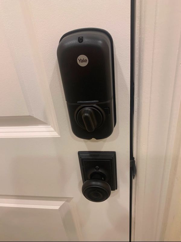 Black Yale smart lock installed on a white door. Lower down is a dark door handle.