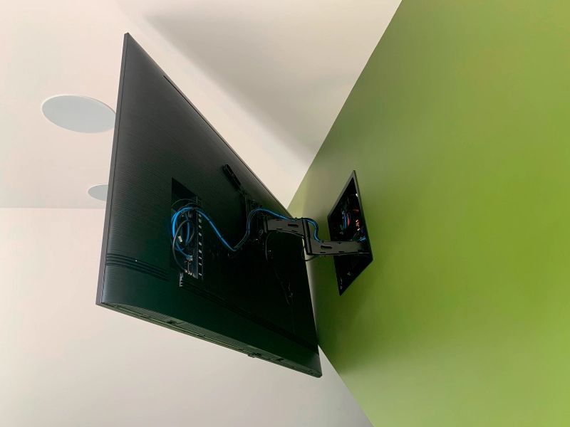 A large TV mounted on an adjustable arm against a green wall, blue cables visible.