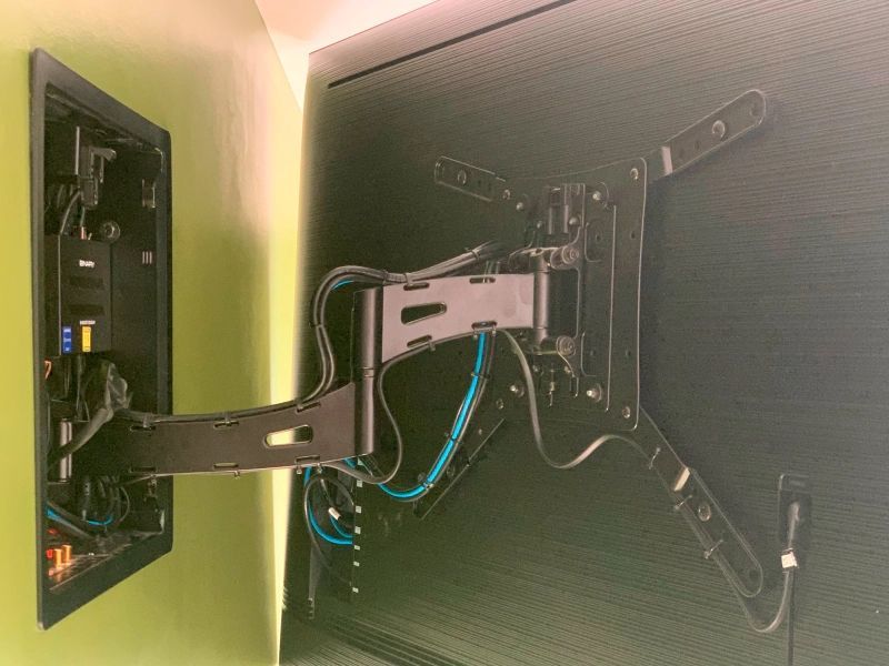 Black TV wall mount with articulated arm, mounted on a wall; exposed wires visible.