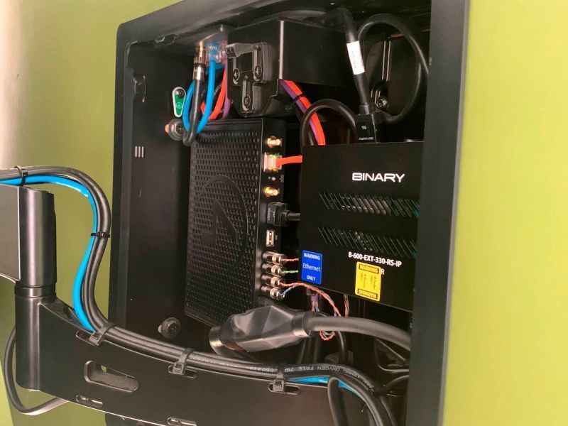 Black electronics box with wires and components mounted on a green wall.