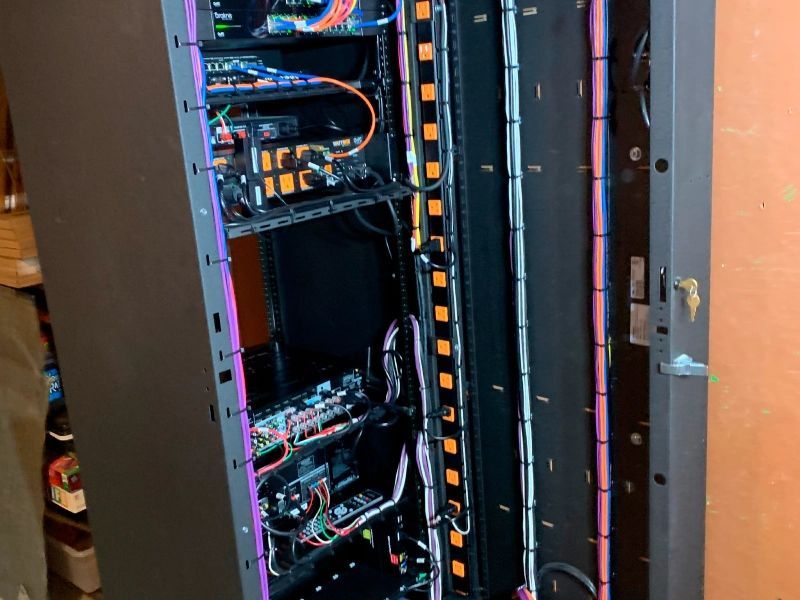 A server rack with various electronic components and cables. The rack is dark gray, with orange and purple cable management.