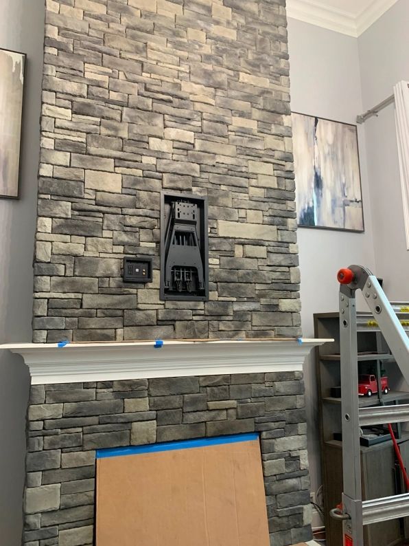 Stone fireplace with a built-in media area; artwork on walls, construction supplies visible.