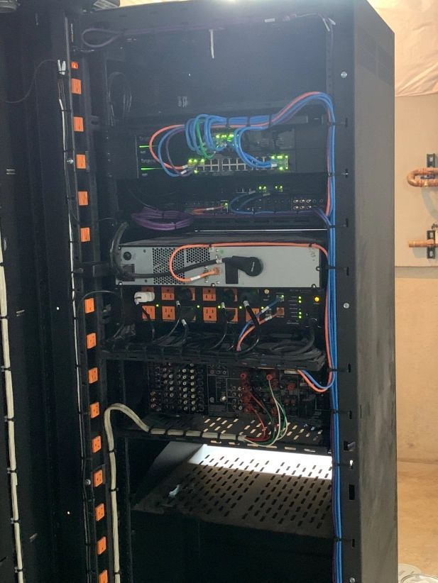 Black server rack filled with electronic equipment and colorful cables.
