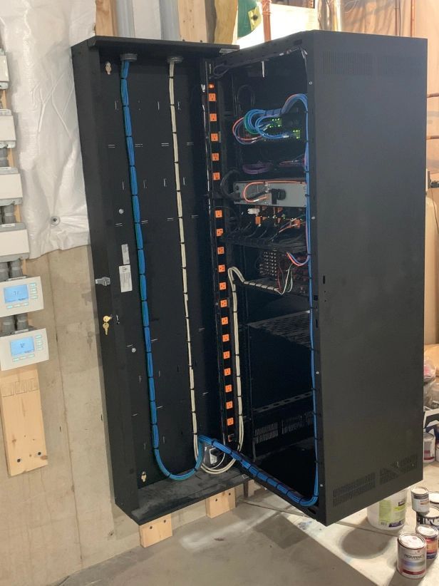 Black server rack cabinet mounted on a wall with open door revealing network equipment and cables.