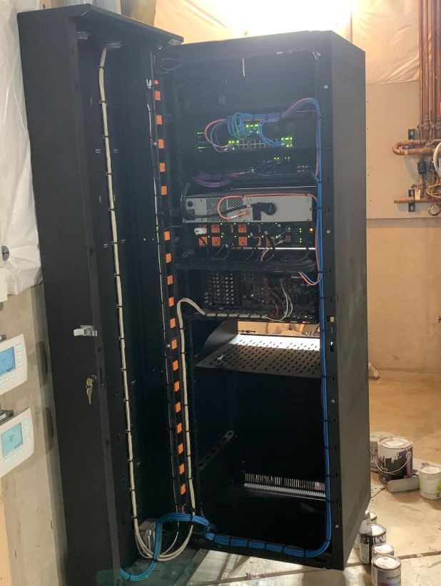 Black server rack with open door, containing electronics and cabling; interior setting.