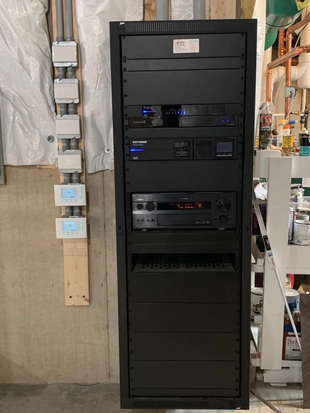 Black AV equipment rack against a beige wall, containing electronic components. Electrical outlets are to the left.