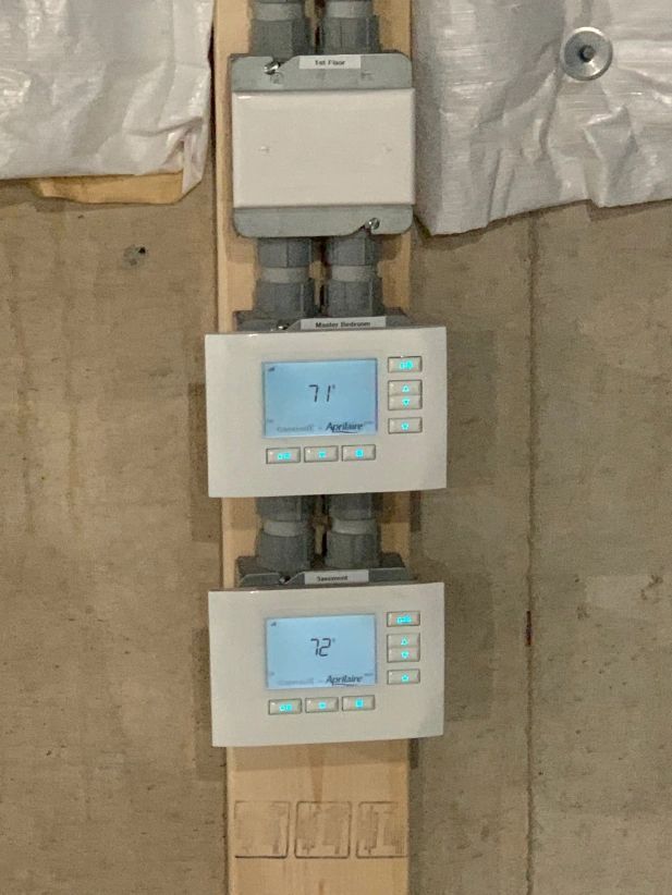 Two white thermostats with illuminated displays and buttons mounted on wooden boards.