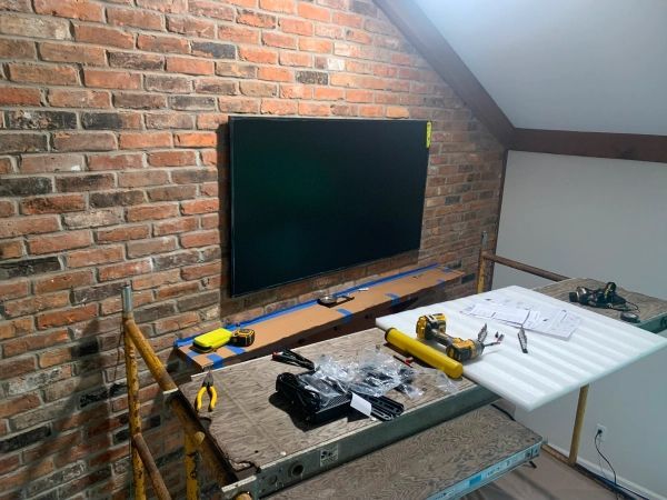 TV mounted on brick wall, tools and workbench nearby. Interior, unfinished space.