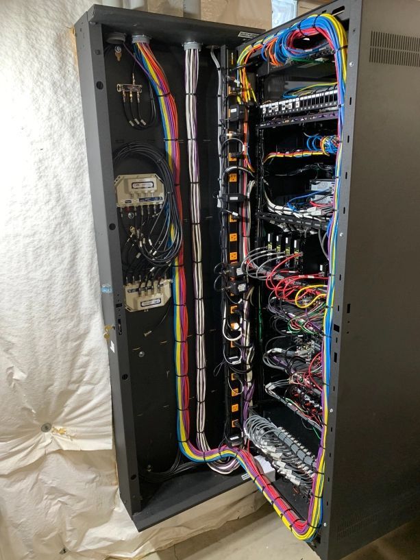 Open server rack with door ajar, filled with colored wires, cables, and electronic components.