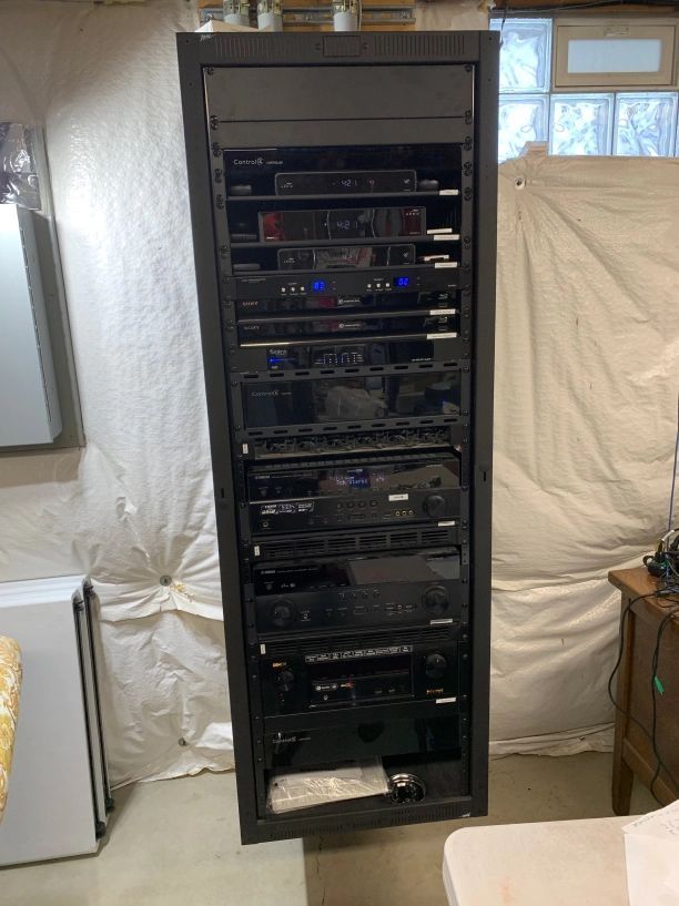 Tall black rack unit with electronic audio/visual equipment against a white wall.