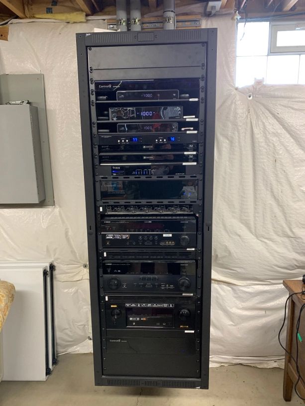 Black rack cabinet filled with AV equipment against a white wall in a basement.
