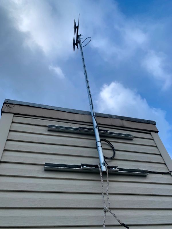 A tall silver TV antenna mounted on the side of a beige house under a cloudy sky.