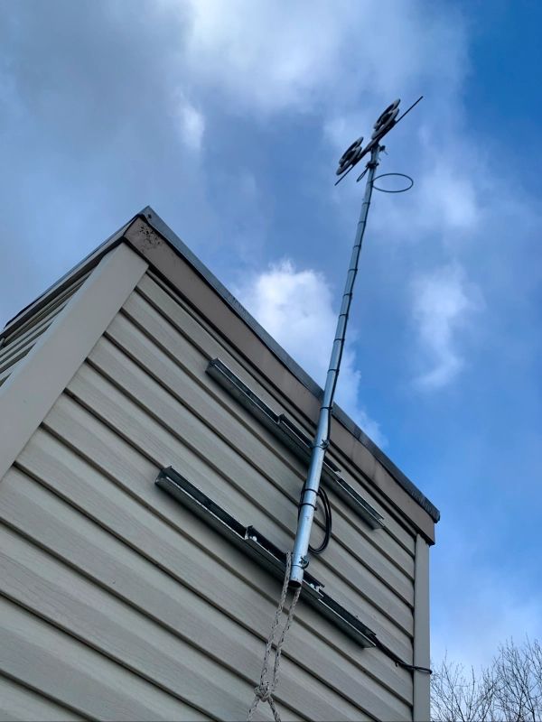 A metal pole with lights and antenna attached to a building's side, against a cloudy sky.