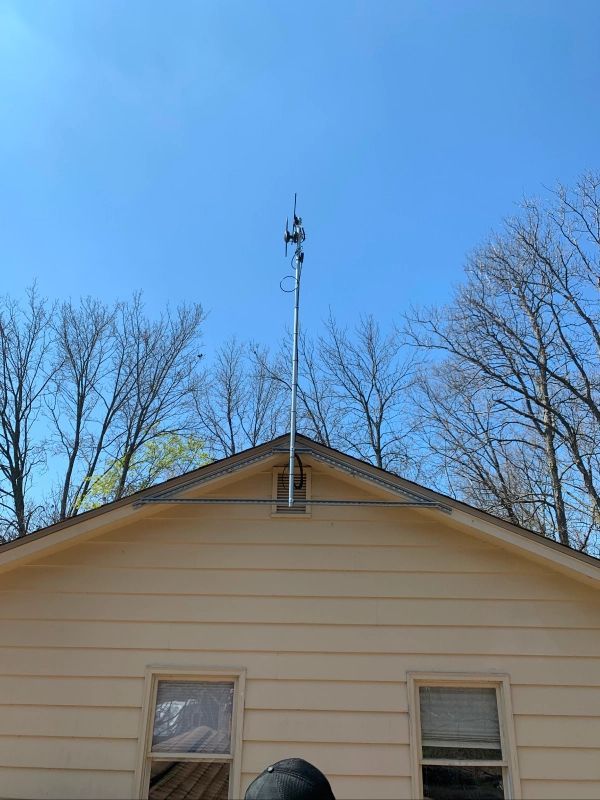 A tall metal antenna pole mounted on a yellow house roof, with antennas at the top and blue sky.