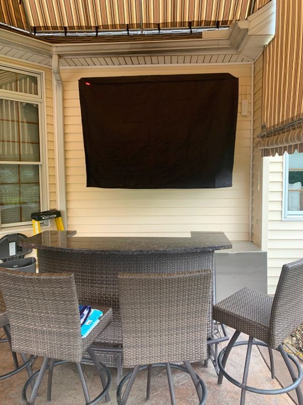 Outdoor patio with a covered TV above a bar with stools.