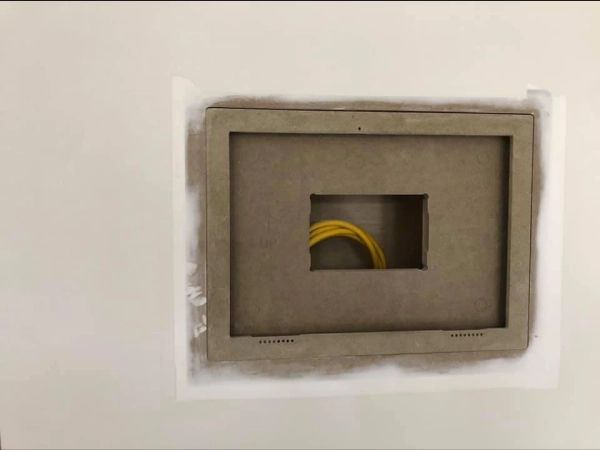 A rectangular wall opening with a brown wooden frame, yellow wires inside. White wall.