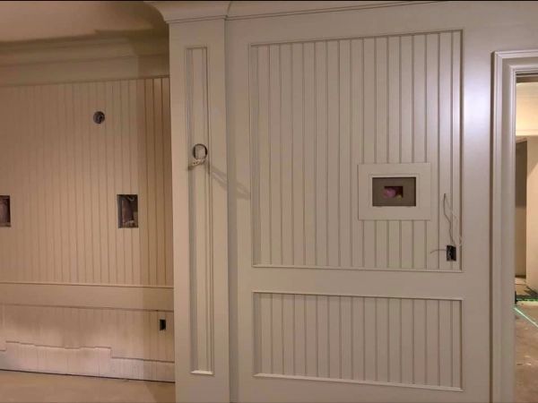 White paneled interior door with hardware and rectangular window, next to a wall with similar paneling.