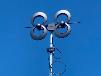Black digital TV antenna against a clear blue sky.