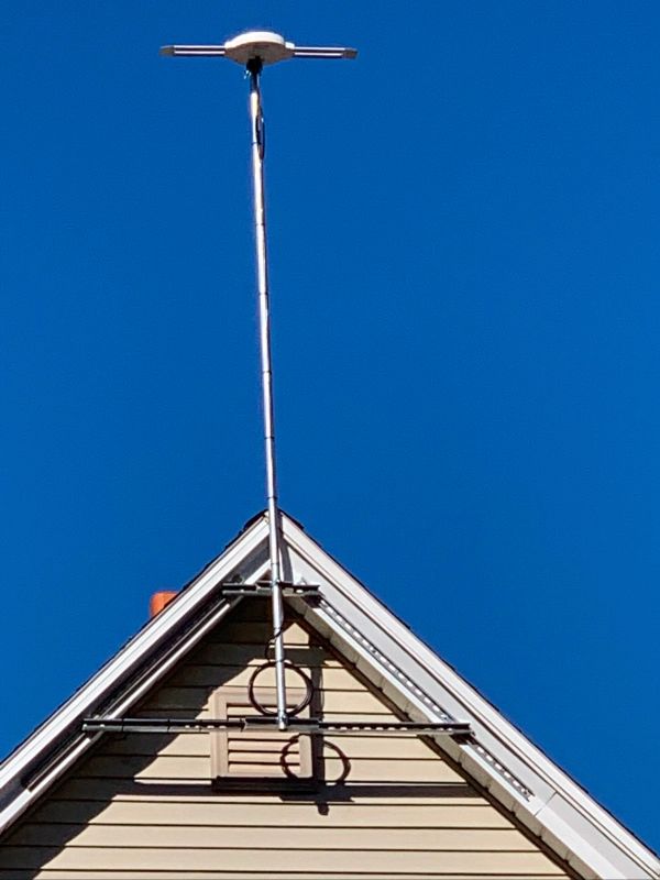 TV antenna mounted on the peak of a house roof, against a bright blue sky.