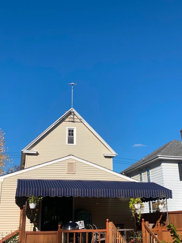 Tan house with blue awning and TV antenna against a bright blue sky.