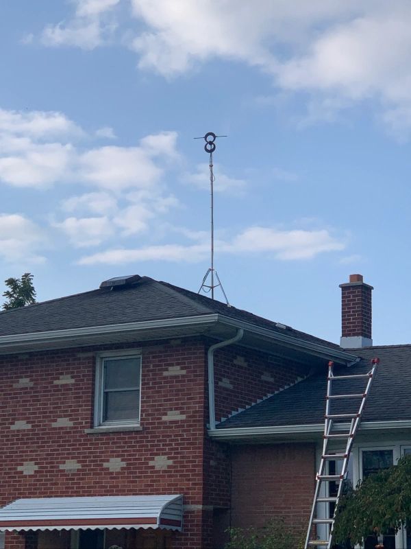 A brick house with a rooftop antenna and a ladder leaning against the side. Blue sky in background.