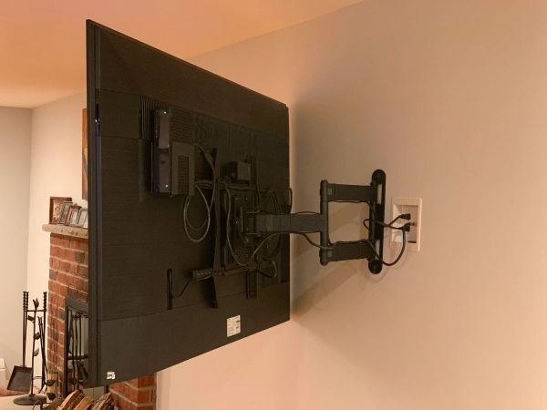 A large flat-screen TV mounted on a wall with a swivel arm, cords, and an electrical outlet.