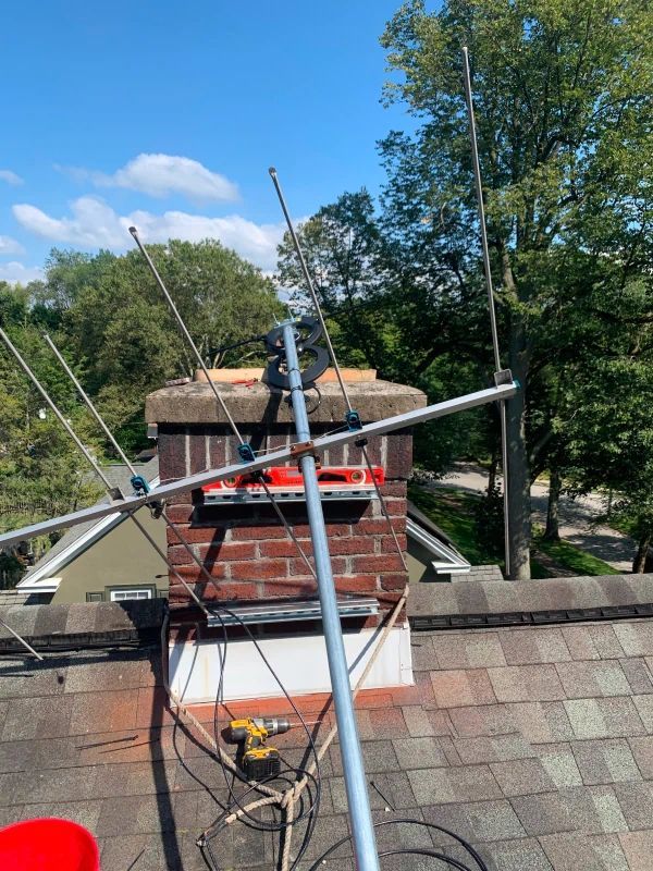 TV antenna mounted on a brick chimney against a blue sky with trees.