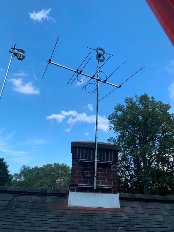 Television antenna mounted on a brick chimney against a partly cloudy blue sky.