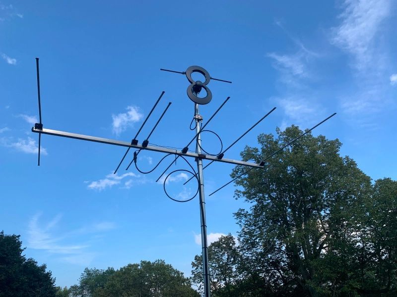 TV antenna against a blue sky, mounted on a pole with a tree in the background.