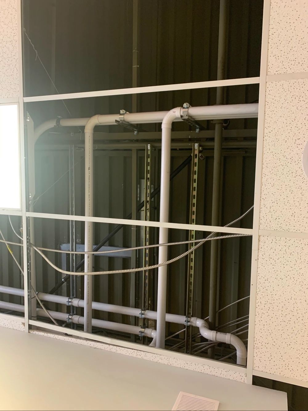 Ceiling tiles removed, revealing pipes and wires above, in a commercial setting.