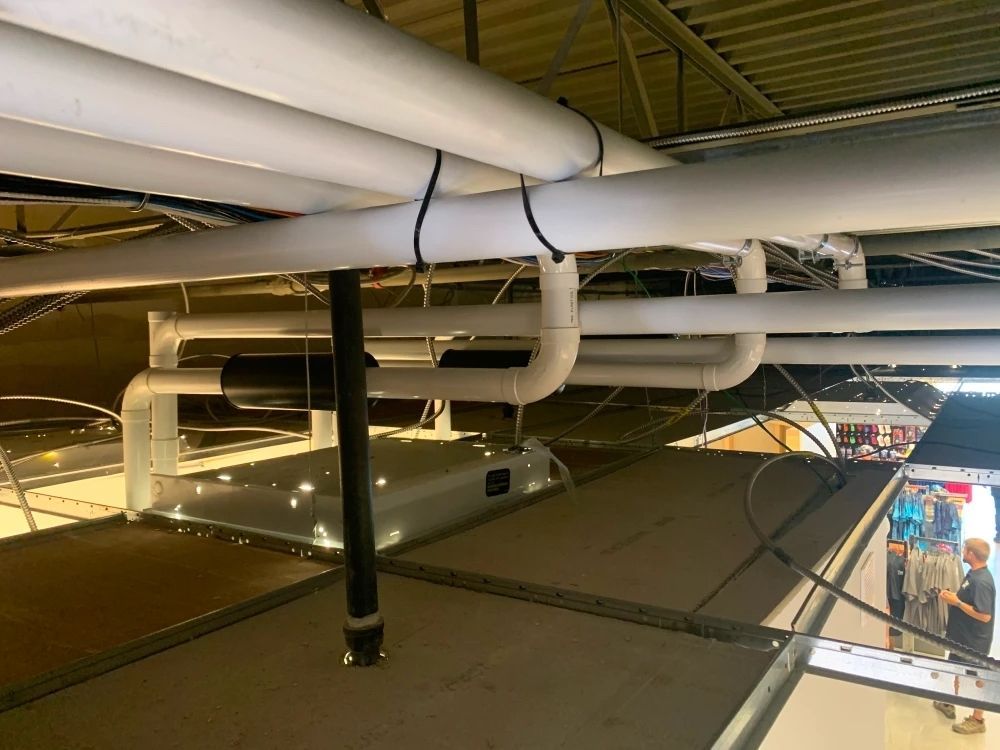 Pipes and ducts installed on a ceiling. Black vertical pipe descends; white horizontal pipes run across.