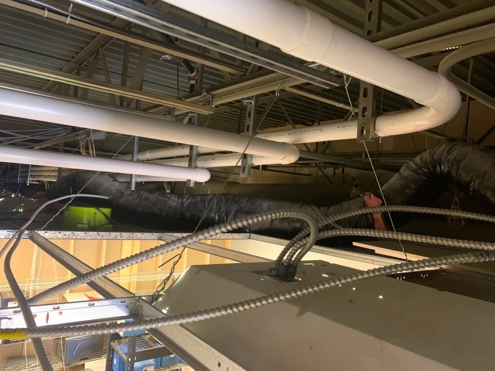 White pipes and metal conduits run across a ceiling, held in place by metal brackets.