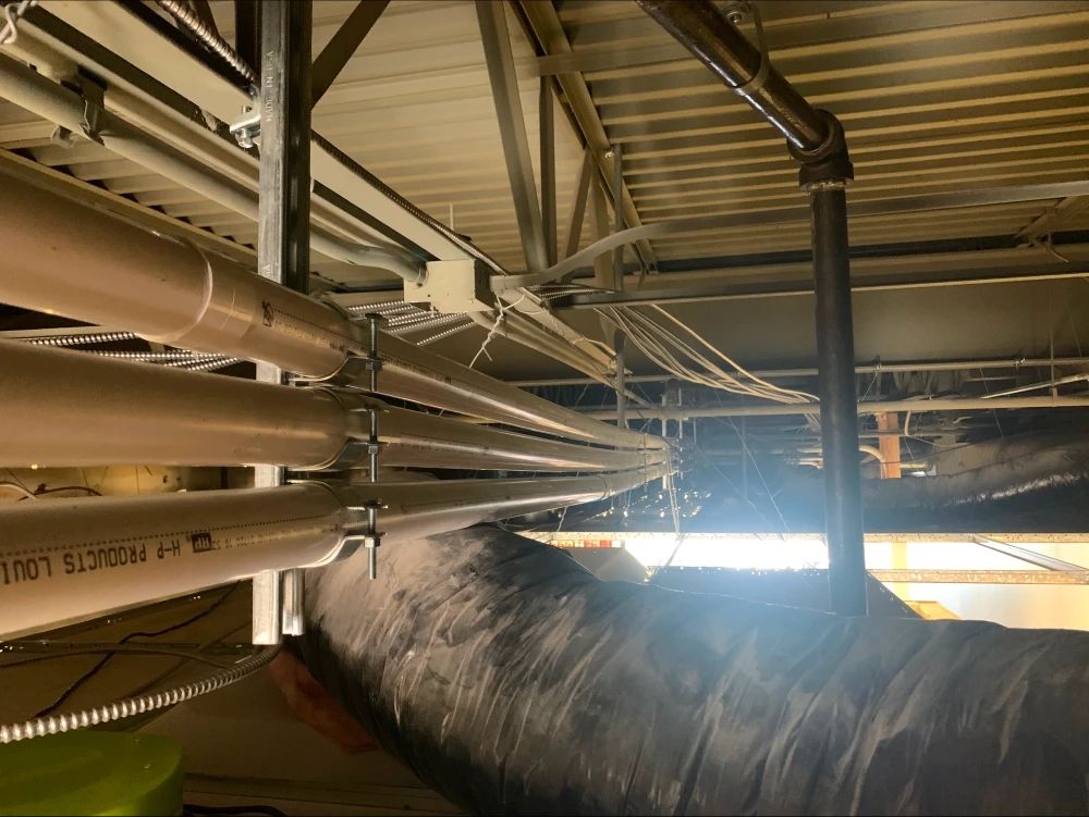 Pipes and wiring running across a ceiling, held in place with metal brackets.