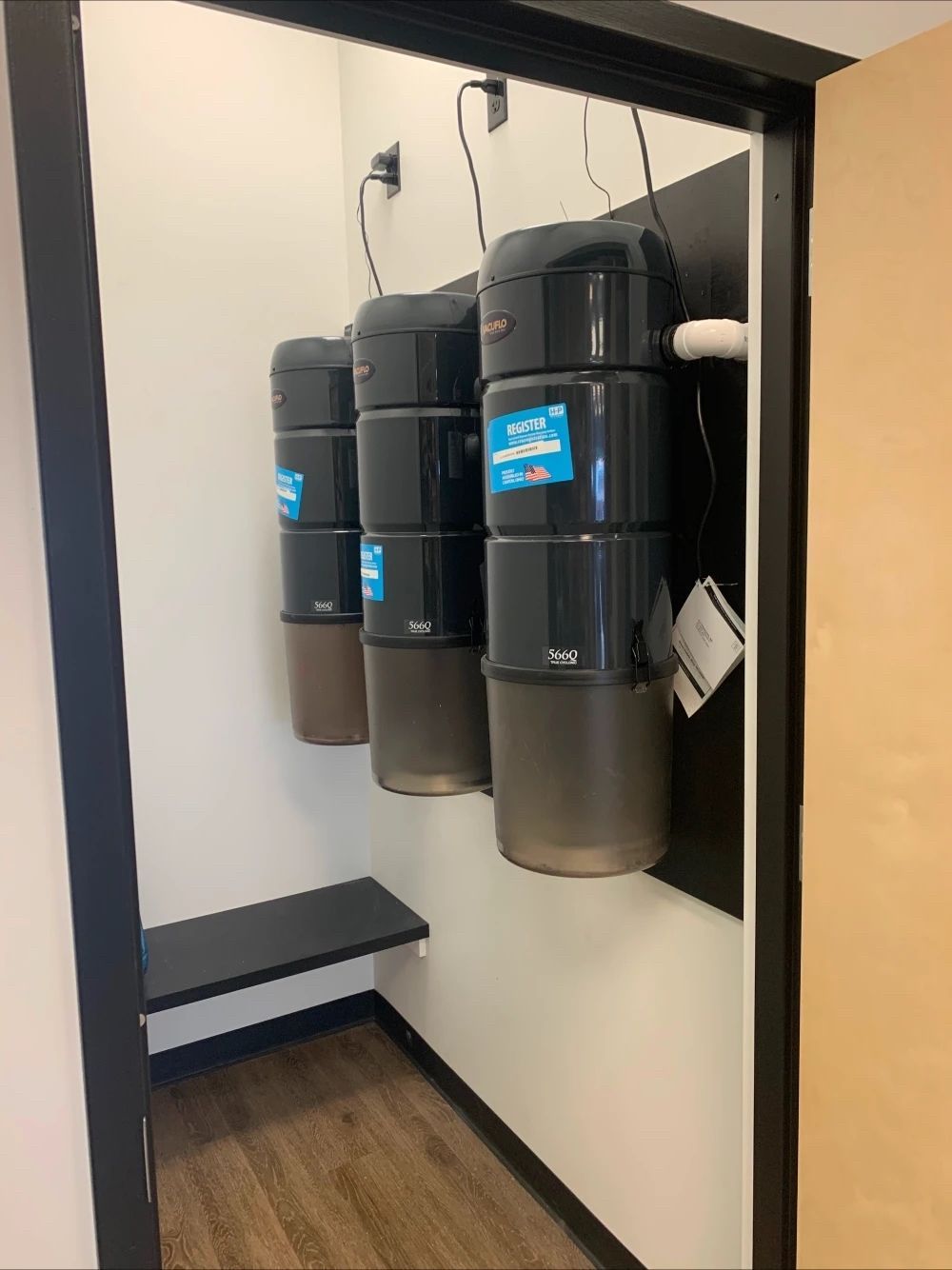 Vacuum canisters mounted on a wall in a small room with a bench.